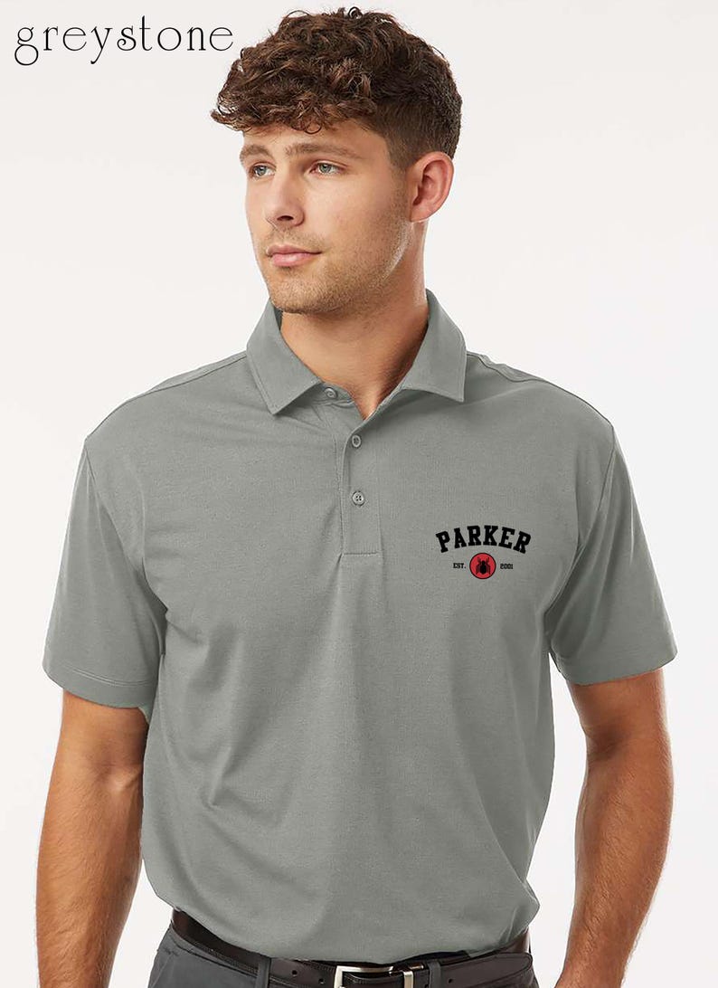 Puede incluir: Un polo gris con cuello y mangas cortas. La camisa lleva la palabra "PARKER" en letras negras sobre un logotipo circular rojo. La palabra "greystone" est&aacute; en la esquina superior izquierda.