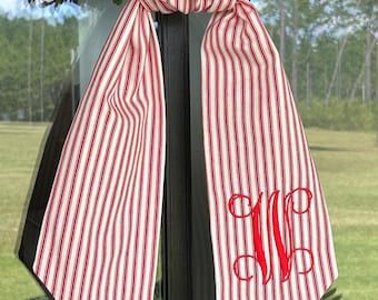 May include: A red and white striped fabric door hanger with a monogram. The fabric has a ticking stripe pattern. The monogram is in red script. The door hanger is hanging on a black door frame.