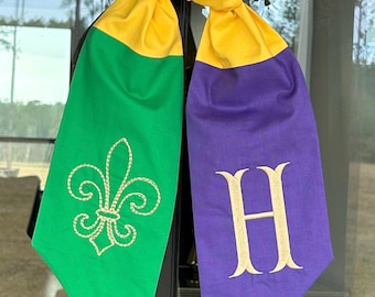 Könnte beinhalten: Ein grüner und violetter Stoff-Türbogen mit goldener Stickerei. Die grüne Seite zeigt eine Fleur-de-lis und die violette Seite den Buchstaben "H".