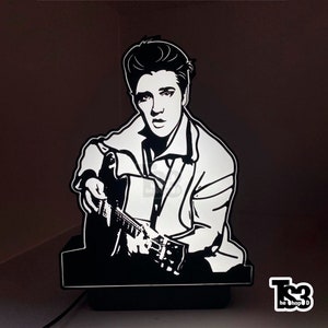 May include: Black and white silhouette of Elvis Presley playing a guitar. The image is a 3D printed lamp with a black base.