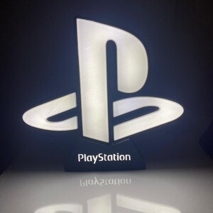May include: A white PlayStation logo light with a black base. The logo is illuminated and the base has the word "PlayStation" printed on it.