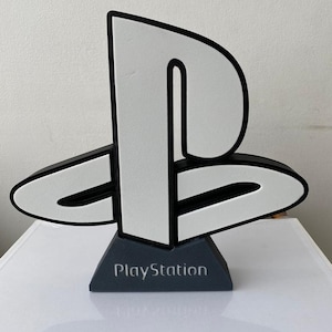 May include: A white PlayStation logo with a black outline, standing on a black base with the word "PlayStation" printed on it.
