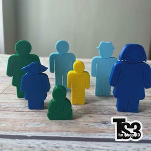 Puede incluir: Una colección de siete figuras de plástico de colores que representan diversas formas humanas, incluyendo adultos y niños en tonos verde, azul, azul claro y amarillo. Las figuras son siluetas planas y estilizadas con cabezas redondeadas.