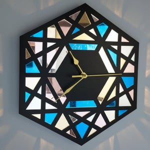 May include: A geometric wall clock with a black hexagonal frame and a black clock face. The clock has gold-coloured hands and mirrored glass inserts in blue, silver, and gold. A decorative item for the home.