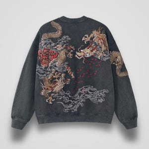 Puede incluir: Una sudadera gris carbón de manga larga con un intrincado diseño bordado de dos dragones dorados entrelazados con detalles florales rojos y motivos de nubes blancas en la espalda. La prenda tiene cuello redondo y puños acanalados.