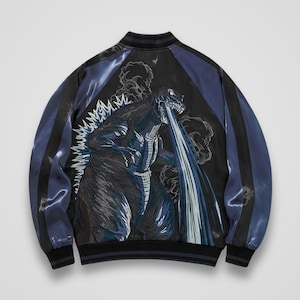 Può includere: Un giubbotto bomber in raso con un grande ricamo di un mostro sul retro. La giacca presenta un pannello centrale nero, maniche blu scuro con strisce nere e colletto, polsini e orlo a coste. Il mostro è raffigurato mentre emette un raggio blu.