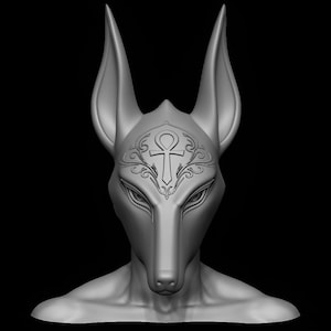 May include: A gray sculpture of a jackal-headed figure, possibly Anubis, with large ears and detailed facial features. An ankh symbol is etched on the forehead, with decorative swirls. The figure is set against a black background.