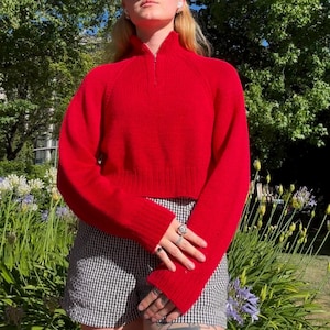 Könnte beinhalten: Ein roter, kurzer Pullover mit Reißverschluss am Kragen. Der Pullover hat lange Ärmel und eine gerippte Struktur.