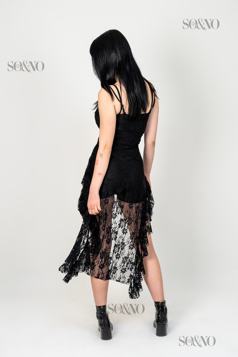 May include: A black lace dress with a sheer skirt and ruffled detailing. The dress has a fitted bodice and a flowing skirt. The model is wearing black heeled boots.