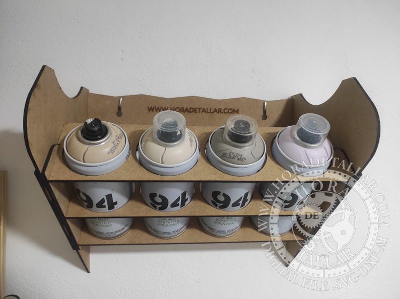 Puede incluir: Un organizador de madera para botes de pintura en aerosol con cuatro botes en cada uno de los dos niveles. Los botes son de color beige, gris y lila claro. La fila inferior de botes tiene el n&uacute;mero "94" impreso. El sitio web "www.horadetallar.com" est&aacute; impreso en la parte superior.