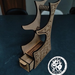 Puede incluir: Una torre de dados de madera con un cajón y un mecanismo de liberación de dados de resorte. La torre está decorada con intrincados tallados y el texto "HORADETALLAR".