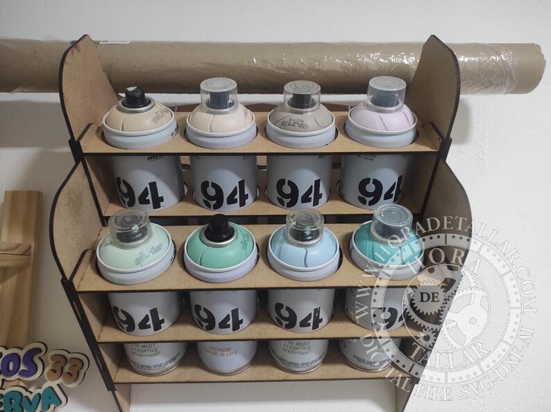 Puede incluir: Un organizador de madera para botes de pintura en aerosol con doce botes. Los botes son blancos con el n&uacute;mero "94" impreso. Las tapas de los botes son de varios colores, incluyendo beige, verde y azul. Un rollo de papel es visible encima del organizador.