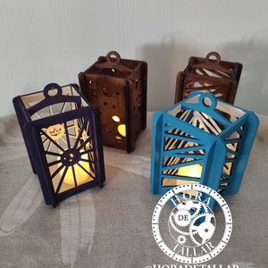 Pode incluir: Quatro lanternas de velas de madeira, cada uma com um design e cor diferentes. As lanternas são pintadas em tons de marrom, azul e roxo. As lanternas são iluminadas por velas, projetando um brilho quente. As lanternas estão dispostas sobre uma superfície marrom claro. A imagem inclui o texto "HORA DE TALLAR" e "@HORADETALLAR".