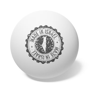 Puede incluir: Una pelota de ping-pong blanca con un sello circular en blanco y negro que dice "Made in Israel" con una silueta del país de Israel dentro del sello.