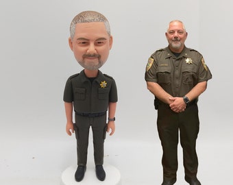 May include: A custom bobblehead figurine of a person wearing a green uniform with a badge and a star. The figurine is standing on a white base. The person is also pictured in a full-length photo wearing the same uniform.