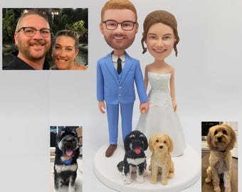 May include: A wedding cake topper featuring a bride and groom in a blue suit and white dress, holding hands. Two dogs, one black and white and one light brown, are standing in front of the couple.