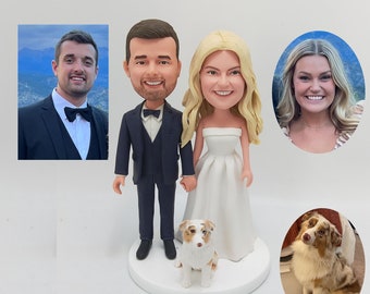 May include: A wedding cake topper featuring a bride and groom in a caricature style, with a dog standing in front of them. The bride is wearing a white dress and the groom is wearing a dark suit. The dog is a brown and white Australian Shepherd.