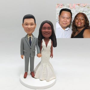 May include: A wedding cake topper featuring a custom-made figurine of a couple in a wedding dress and suit. The couple is holding hands and smiling.
