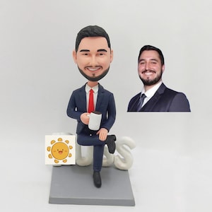 May include: A custom bobblehead figurine of a person wearing a blue suit and red tie, holding a white coffee mug. The figurine is sitting on a gray base with the word "Boss" written in white letters.