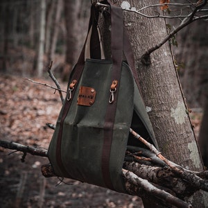 May include: A green canvas bag with brown leather straps and a brown leather patch that says "PALAY" hanging from a tree branch. The bag is filled with sticks.