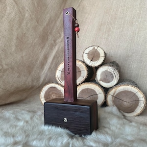 May include: A dark red wooden mallet with a handle that has the text "YINPALAWOODWORKS" engraved on it. The mallet is sitting on a white faux fur surface with a stack of wooden logs in the background.