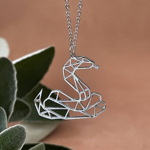 May include: A silver necklace with a geometric snake pendant. The snake is made of interconnected triangles and is in a coiled position.