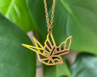 Könnte beinhalten: Eine goldfarbene Halskette mit einem geometrischen Origami-Vogel-Anhänger. Der Anhänger ist aus dünnem Metall gefertigt und hat ein filigranes, kompliziertes Design.