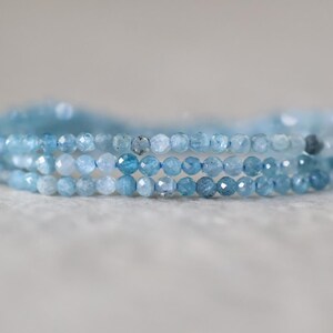 Puede incluir: Una pulsera de tres hilos compuesta por peque&ntilde;as cuentas de piedras preciosas facetadas de color azul claro. Las cuentas muestran tonos variados de azul cielo transl&uacute;cido y cian p&aacute;lido, dispuestas en tres filas paralelas superpuestas.
