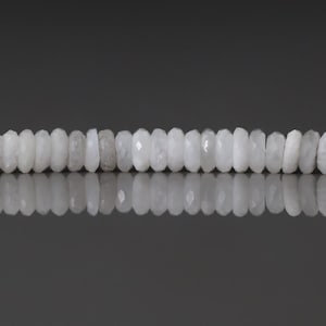 May include: A strand of white, faceted gemstone beads. The beads are a soft, opaque white color and have a slightly irregular shape. The beads are strung together, creating a necklace or bracelet.
