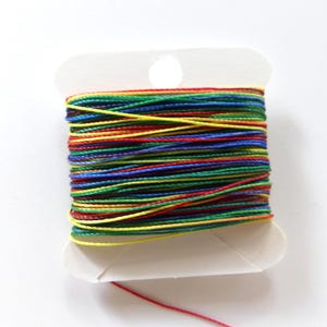 May include: A spool of colorful thread, featuring a vibrant array of colors including red, yellow, green, blue, and purple. The thread is tightly wound on a white cardboard spool, with a single strand of red thread extending from the bottom.