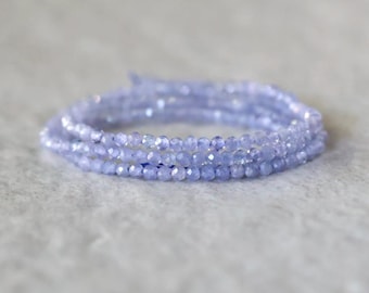 Könnte beinhalten: Ein mehrsträngiges Armband aus kleinen, facettierten, hellen, immergrün-blauen Perlen. Die Perlen sind in einer kreisförmigen, gewickelten Formation angeordnet und reflektieren das Licht auf ihren zahlreichen geschliffenen Oberflächen.