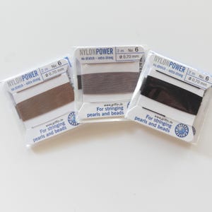 May include: Three spools of nylon beading thread in brown, gray, and black. Each spool is labeled "NYLONPOWER" and includes the text "For stringing pearls and beads." The thread is 2 meters long and 0.70 mm in diameter.