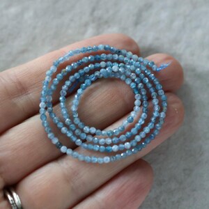 Puede incluir: Una hebra enrollada de peque&ntilde;as cuentas de piedras preciosas facetadas de color azul claro. Las cuentas muestran tonos variados de azul transl&uacute;cido, desde el azul cielo p&aacute;lido hasta tonos azur m&aacute;s profundos, ensartadas en un hilo azul claro.