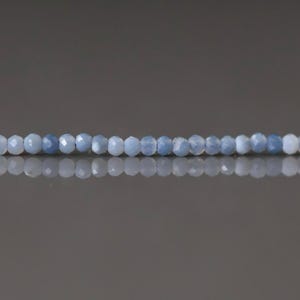 May include: A strand of faceted, light blue gemstone beads. The beads are small, round, and evenly spaced, reflecting light. The background is a gradient of gray.