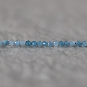 Puede incluir: Un solo hilo de peque&ntilde;as cuentas redondas facetadas en varios tonos de azul, que van desde el azul cielo claro hasta el azul oc&eacute;ano profundo. Las cuentas est&aacute;n ensartadas en una l&iacute;nea horizontal, mostrando una calidad transl&uacute;cida y brillante.