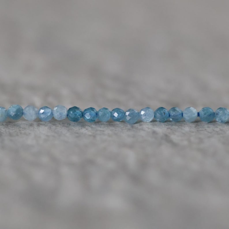 Puede incluir: Un solo hilo de peque&ntilde;as cuentas redondas facetadas en varios tonos de azul, que van desde el azul cielo claro hasta el azul oc&eacute;ano profundo. Las cuentas est&aacute;n ensartadas en una l&iacute;nea horizontal, mostrando una calidad transl&uacute;cida y brillante.