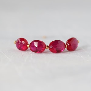 May include: A horizontal arrangement of four faceted, oval-shaped, vibrant pink gemstones. The stones are linked together in a row, separated by small, polished gold-toned metal beads between each gem, creating a delicate and symmetrical jewelry component.