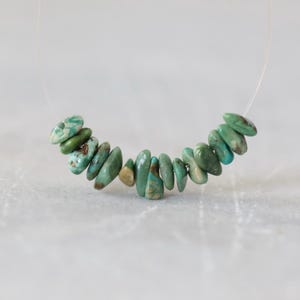 May include: A strand of small, irregular, tumbled turquoise gemstone beads in shades of teal, seafoam green, and light blue with brown matrix inclusions, strung on a thin, clear, flexible filament wire for jewelry making and crafting.
