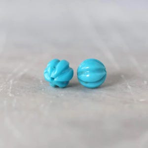 May include: Two round, bright turquoise beads with a distinct ribbed or melon-like texture. Each bead features a smooth, glossy finish and a central hole, showcasing a vibrant blue-green color and a symmetrical, segmented spherical shape.