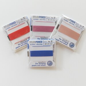 May include: Four spools of nylon string in red, mauve, peach, and blue. Each spool is labeled "NYLONPOWER" and includes the diameter in millimeters. The packaging reads "For stringing pearls and beads."