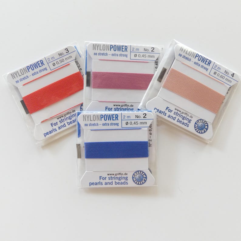 May include: Four spools of nylon string in red, mauve, peach, and blue. Each spool is labeled "NYLONPOWER" and includes the diameter in millimeters. The packaging reads "For stringing pearls and beads."