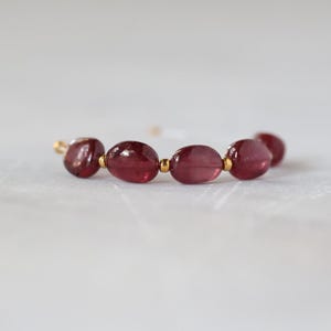 May include: A bracelet featuring a series of smooth, oval-shaped deep red garnet beads. The garnet stones are separated by small, polished gold-toned metal spacer beads, creating a repeating pattern along the length of the jewelry piece.