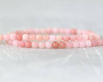 Puede incluir: Una pulsera delicada compuesta por pequeñas cuentas redondas y lisas en varios tonos de rosa suave. Las cuentas están ensartadas en un bucle continuo, mostrando un tamaño uniforme y un acabado pulido y semitranslúcido en toda la pieza.