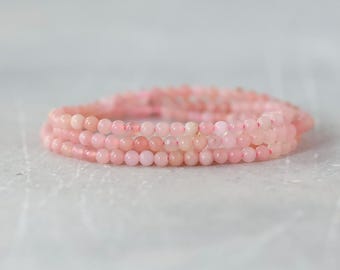 Puede incluir: Una pulsera de múltiples hilos compuesta por pequeñas cuentas redondas y lisas en varios tonos de rosa suave. Las cuentas están ensartadas en un bucle continuo, creando una apariencia delicada y uniforme con un acabado pulido en toda la pieza.