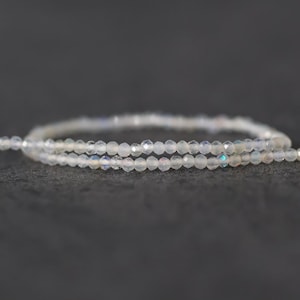 May include: A strand of small, translucent, faceted beads with an iridescent sheen. The beads are strung together in a continuous line, displaying subtle light reflections and a clear, glass-like appearance throughout the entire length of the strand.