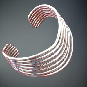 May include: A silver bangle bracelet with a multi-layered design. The bracelet is made of multiple thin bands of metal that are woven together to create a unique and stylish look.