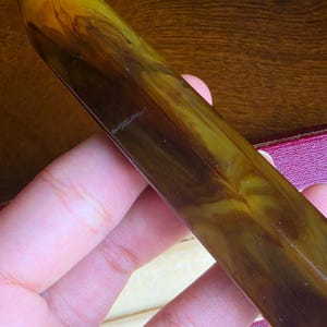 May include: A cylindrical writing instrument featuring a polished, marbled finish with swirling patterns of dark brown and olive green. The surface is smooth and glossy, displaying a continuous, organic blend of these two earthy tones throughout.