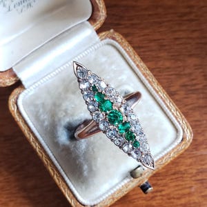 May include: A vintage ring with a pointed design set with emerald and diamond stones. The ring is in a small, velvet-lined box.