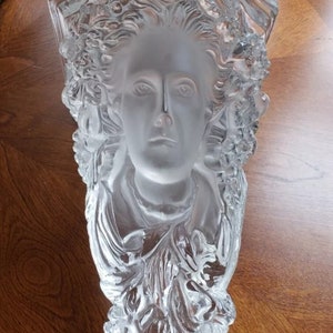 May include: A clear glass wall sculpture with a detailed design of a woman's face surrounded by floral motifs.