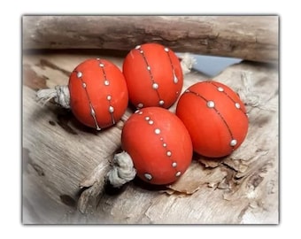May include: Four orange decorative spheres with white accents and string attachments. The spheres are arranged on a piece of driftwood, creating a rustic and natural aesthetic. The spheres have a dotted pattern and a line of white accents.